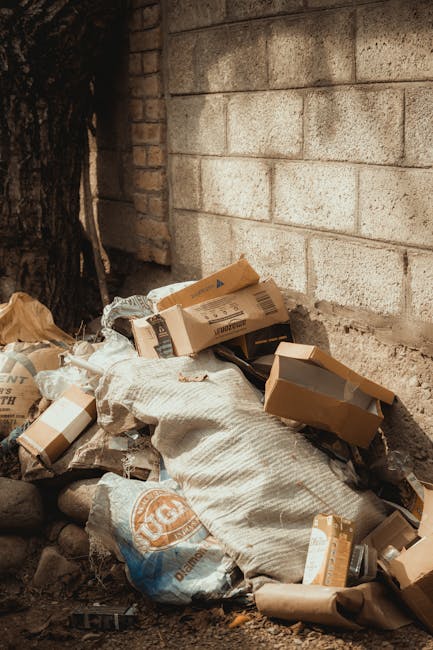 A photograph showing a collection of various types of rubbish placed on a driveway or paved outdoor area. The waste includes a large, black plastic bag filled with debris, lying flat on the ground. Ne